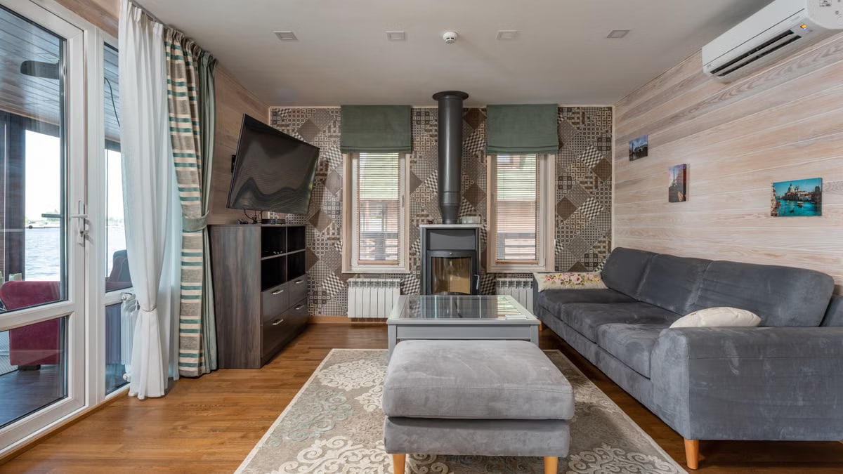 Modern design of country house with light wooden walls and carpet with ornament on parquet and dark gray furniture and curtains on wide balcony door and narrow windows